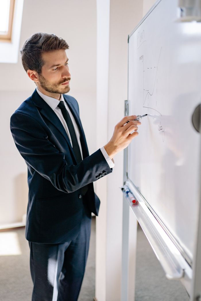 Confident businessman in a blue suit presenting analytics on a whiteboard.